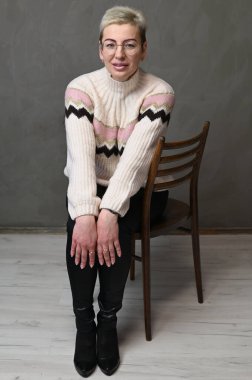 Saçları kısa saçlı, gri bir arka planda gülümseyen yetişkin, beyaz bir kadın.