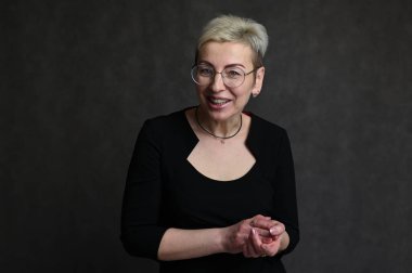 Gri arka planda gözlüklü, beyaz tenli, sarışın bir kadının portresi.