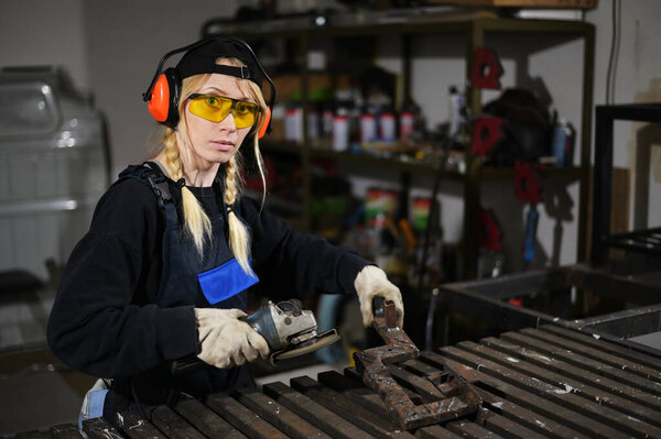 Photo of a caucasian girl working with an angle grinder in a mask at production