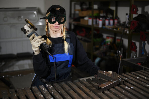 Photo of a caucasian girl working with an angle grinder in a mask at production