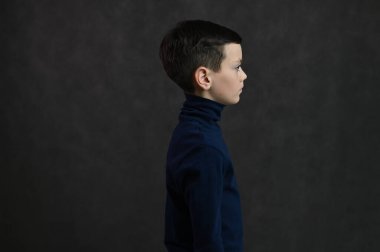 Gri arka planda esmer, esmer, ciddi bir çocuğun yan görüntüsü.