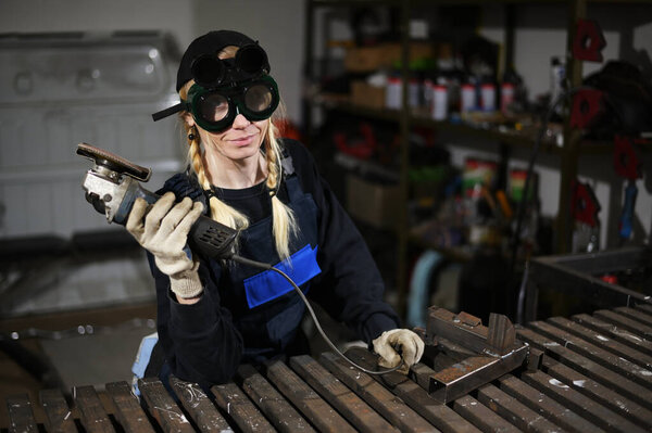 Photo of pretty woman in overalls holding an angle grinder