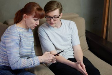 Odadaki kanepede oturan anne ve oğlunun telefonda konuştuğu fotoğraf.