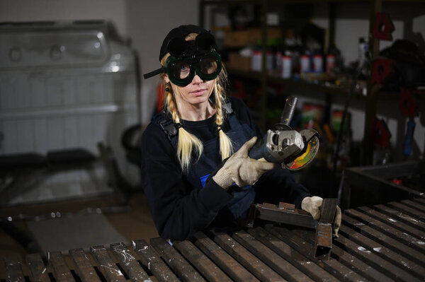 Photo of woman with angle grinder works in protective clothing at production