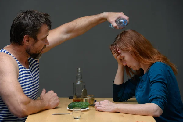 一个成年男子坐在桌旁戏弄一个女人 因酗酒引起的家庭问题而被收养 — 图库照片
