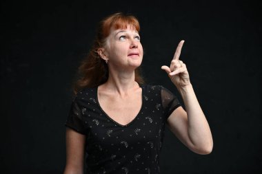 Gülümseyen yetişkin bir kadının portresi siyah arka planda bir parmağı gösteriyor.