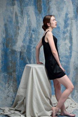 Slim model in black dress in studio posing standing on blue background