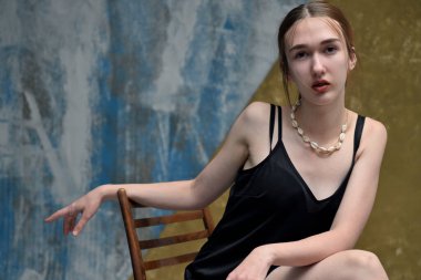 Young slim woman in studio posing while sitting on a chair on a colorful background