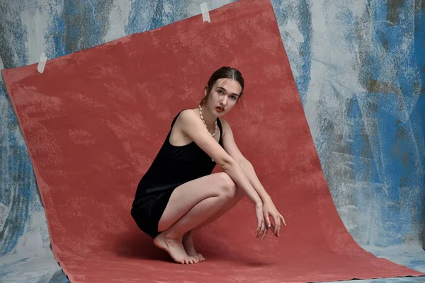 Young woman in studio posing while sitting on floor on pink colorful background