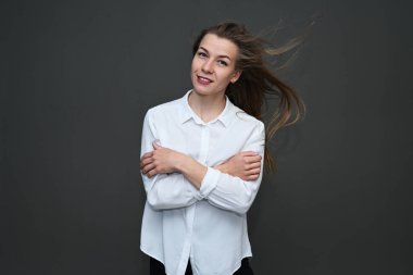 Beyaz tişörtlü, gri arka planda dalgalı saçları olan neşeli beyaz bir kızın portresi..
