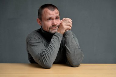 Orta yaşlı bir adam gülümseyerek masada otururken yan tarafa bakar.