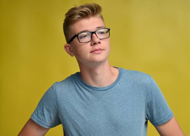 Gözlüklü, sevimli, beyaz bir gencin portresi. Gülümseyen, sarı arka plandaki mesafeye bakan.