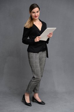 İş kadını portresi, iş elbisesi içinde, elinde bir klasörle gri bir arka planda gülümsüyor.