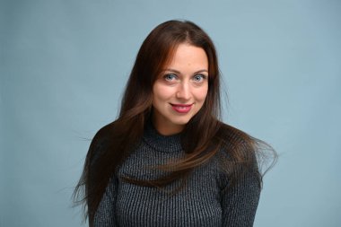 Stüdyoda gülümseyen beyaz kadın mavi arka planda uçan saçlarla poz veriyor.