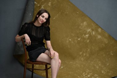 Esmer kız bej arka planda, stüdyoda bir sandalyede oturuyor.