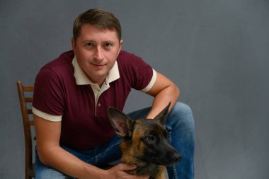 Belçikalı çoban Malinois ile yakışıklı adam gri arka planda stüdyoda kameraya bakıyor.