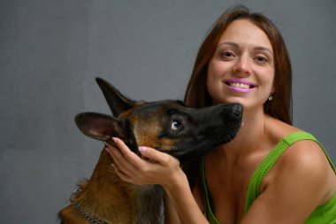 Gri bir arka planda, elinde köpekle kameraya bakan gülümseyen bir kızın resmi.