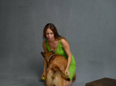 Gri bir arka planda resim. Şirin, narin bir kız köpekle oynuyor.