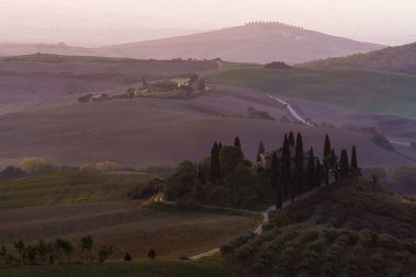 İtalya 'da bir selvi çiftlik evi ve saman balyalarıyla altın sabah ışığında güzel bir Toskana tarlası manzarası. Val dOrcia