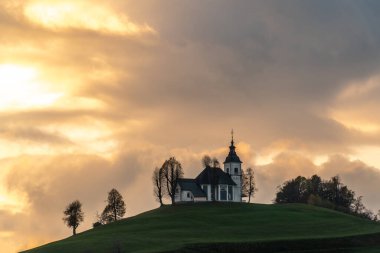 Bulutlu havada renkli bir gün batımı. Kilisenin manzarası Sv Sobota. Slovenya sonbaharda