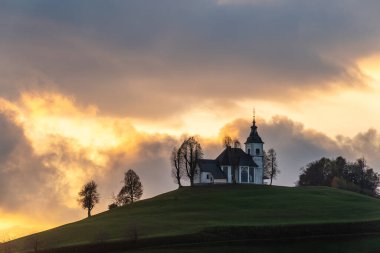 Bulutlu havada renkli bir gün batımı. Kilisenin manzarası Sv Sobota. Slovenya sonbaharda
