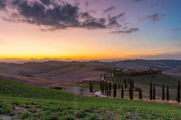 Toskánsko, venkovská krajina při západu slunce. Venkovská farma, cypřiše, zelené pole, sluneční svit a mraky. Itálie, Evropa. — Stock fotografie
