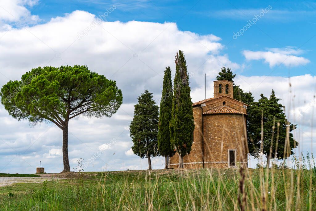 A chapel with cypresses in the center of the field. Church on a hill and green surroundings. Chapel of the Madonna di Vitaleta, Siena, Tuscany, Italy.