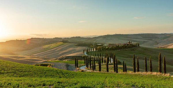 Знаменитый тосканский пейзаж с полями, кипарисами и домами на закате. Осенний сельский пейзаж с извилистой дорогой в Тоскане, Италия, Европа.