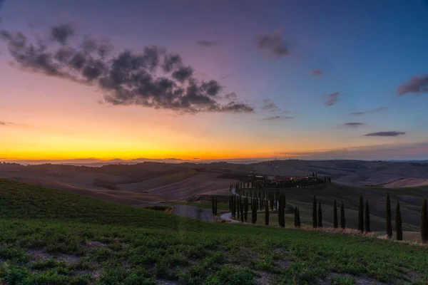 Toszkána, vidéki táj naplementekor. Vidéki gazdaság, ciprusok, zöld mezők, napsütés és felhők. Olaszország, Európa. — Stock Fotó