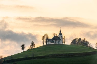 Bulutlu havada renkli bir gün batımı. Kilisenin manzarası Sv Sobota. Slovenya sonbaharda