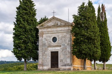 Tarlanın ortasında selvi çiçekleri olan bir şapel. Tepedeki kilise ve yeşil çevre. Madonna di Vitaleta Şapeli, Siena, Toskana, İtalya.