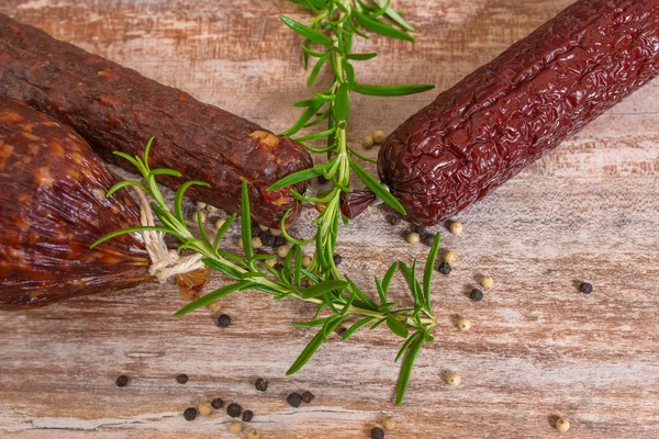 Smoked salami on wooden table with rosemary — Stock Photo, Image