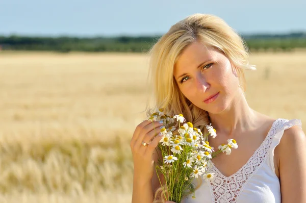 Gelukkige vrouw poseren met kamille in gouden tarwe. — Stockfoto