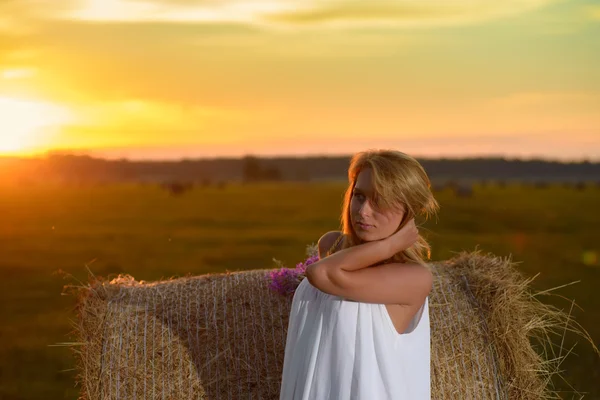 Blond kvinna poserar vid solnedgång på ett fält — Stockfoto