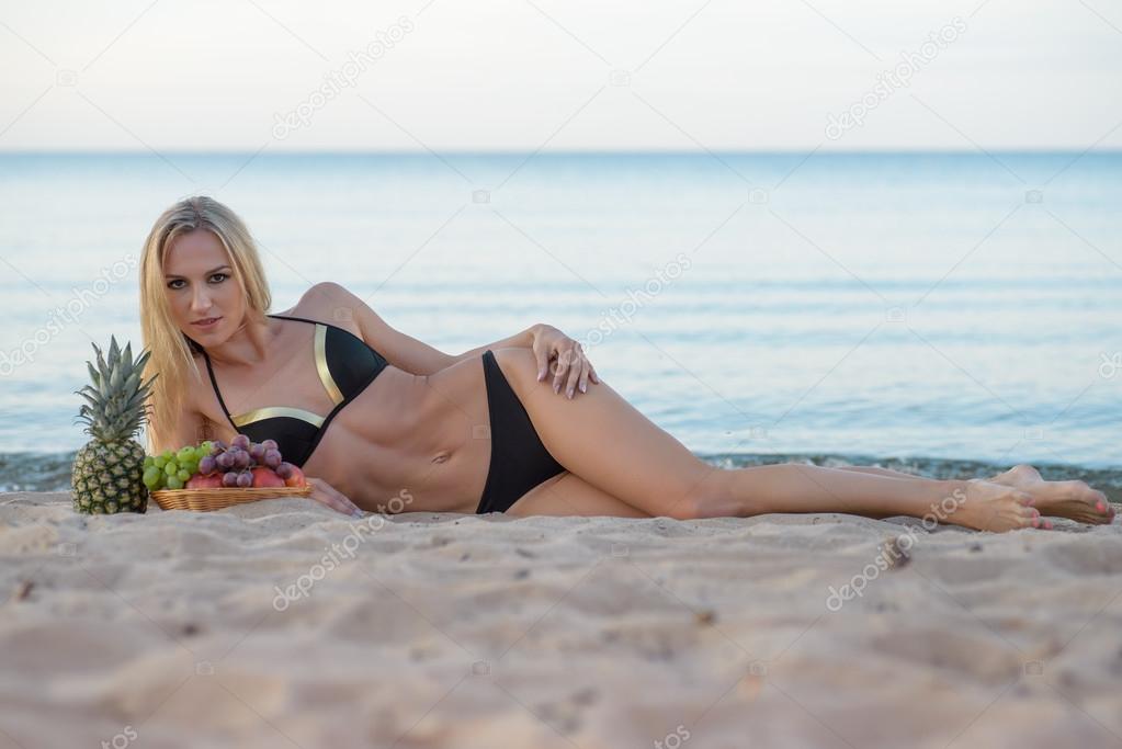 woman in  bikini relaxing on the sand with fruits