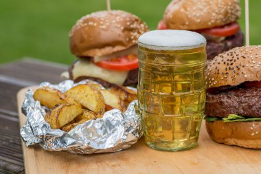 Lezzetli ızgara hamburger, kızarmış patates ve bardak bira.