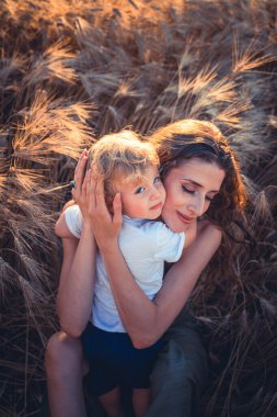 Küçük güzel çocuk buğday tarlasında annesine sarılıyor.