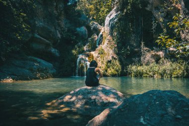 Güneşli bir günde küçük bir şelalenin manzarasına bakan bir kız.