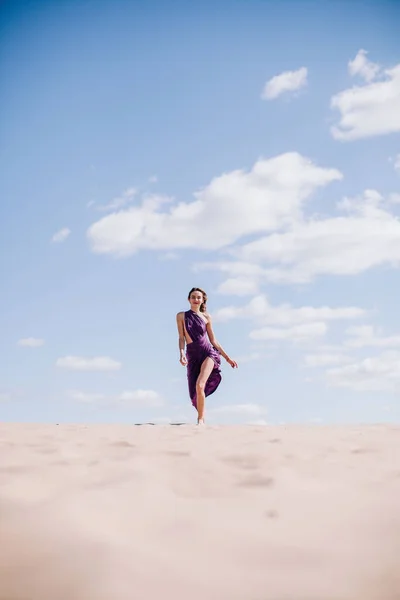 Una chica joven y delgada en un vestido beige con paño púrpura en las manos posando en el desierto en el viento — Foto de Stock