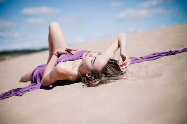 Молода струнка дівчина з фіолетовими позуваннями тканини в пустелі — стокове фото