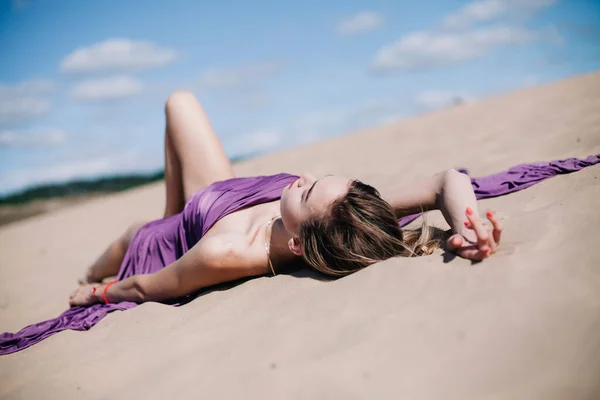Fiatal, karcsú lány lila ruhával pózol a sivatagban. — Stock Fotó