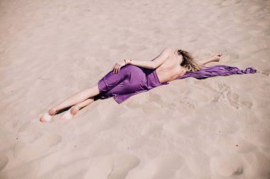 Çölde mor elbiseli genç, narin bir kız poz veriyor.