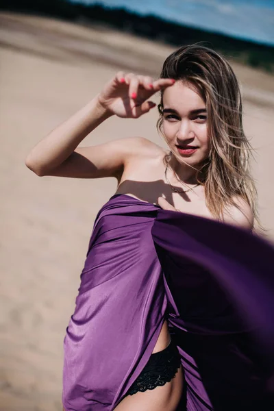 Chica joven y delgada con paño púrpura posa en el desierto — Foto de Stock