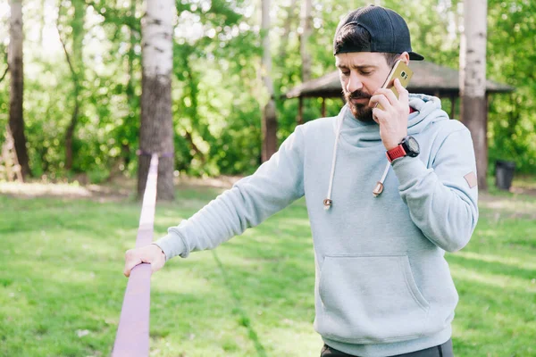 젊고, 운동 선수에 수염을 기른 남자의 사진이 slackline 근처의 파란 후드를 입은 남자 — 스톡 사진