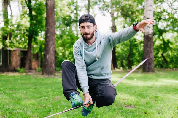 Jovem homem equilibrando e pulando em slackline. — Fotografia de Stock