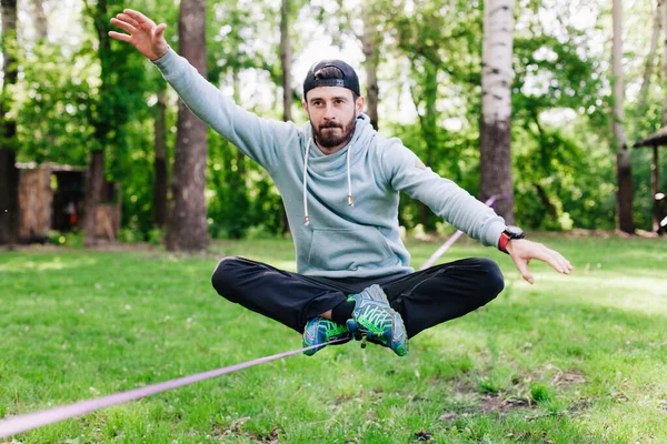 Jovem homem equilibrando e pulando em slackline. — Fotografia de Stock