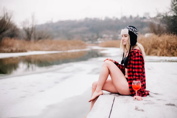 A girl in a swimsuit and a hat with a glass in her hand poses in winter in the cold — Stock Photo, Image