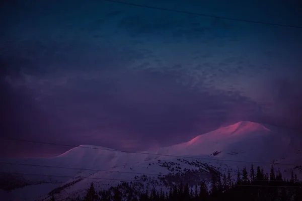 Os primeiros raios do sol ao amanhecer tocam os picos cobertos de neve das montanhas — Fotografia de Stock