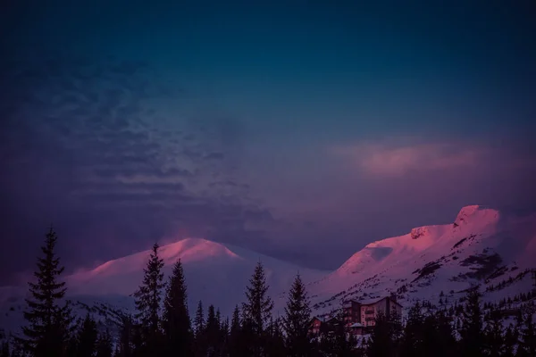 De eerste zonnestralen bij zonsopgang raken de besneeuwde toppen van de bergen — Stockfoto