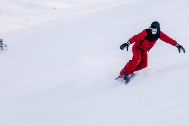 Kırmızı tulumla kayak yapan bir adam yokuştan aşağı kayıyor.